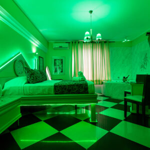 Habitación decorada con iluminación verde, cama doble y un diseño moderno con suelo de cuadros en blanco y negro, ideal para una experiencia vibrante y única.