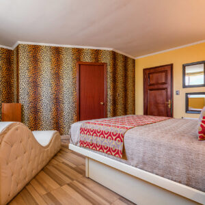 Habitación con cama doble, decoración en tonos cálidos y detalles en estampado animal print, con sillón del amor y televisión de pantalla plana.